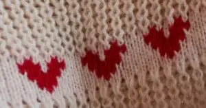 Close-up of a knitted fabric featuring red heart patterns on a soft beige background.